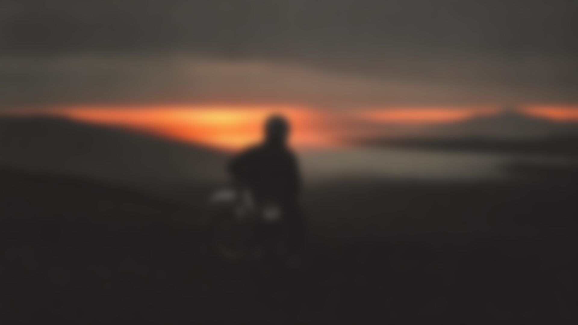 A rider in a crash helmet beside a motorcycle at a moorland viewpoint at sunrise, looking out over a misted valley.